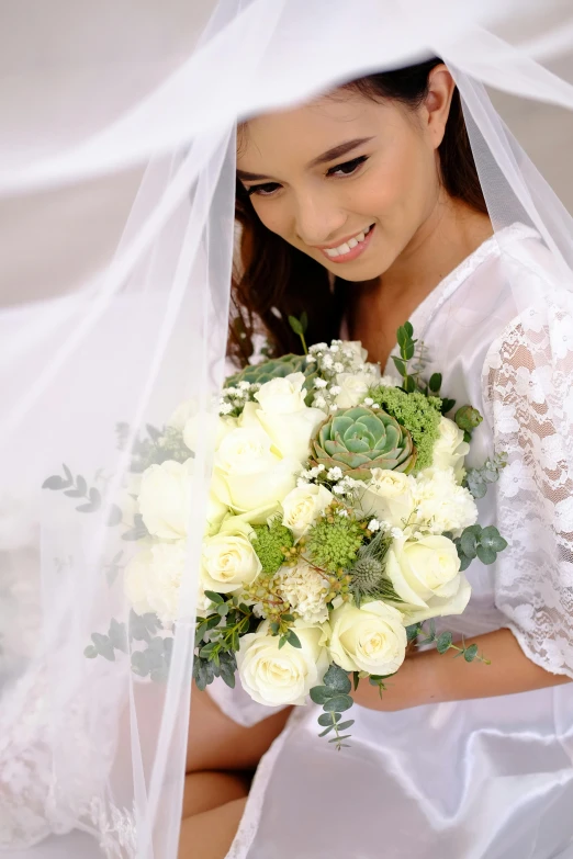 a bride sitting down holding a bouquet under her veil