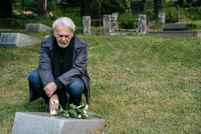 a man in a cemetery kneeling down to a tombstone