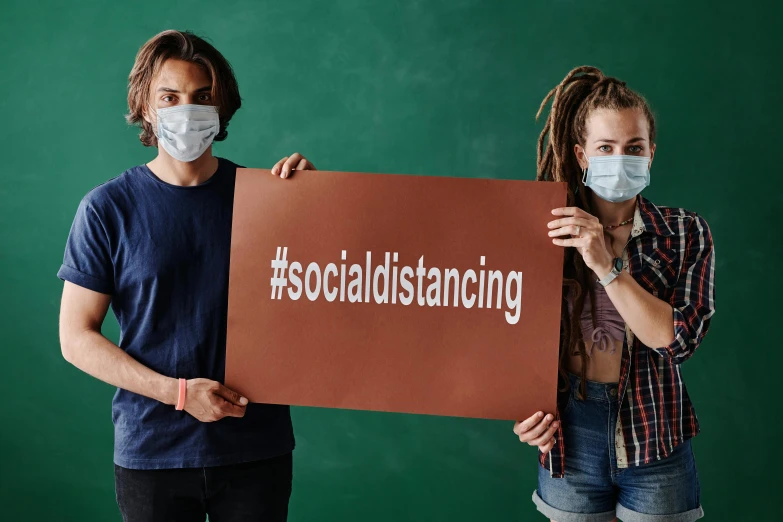 man and woman holding up a cardboard social distancing sign