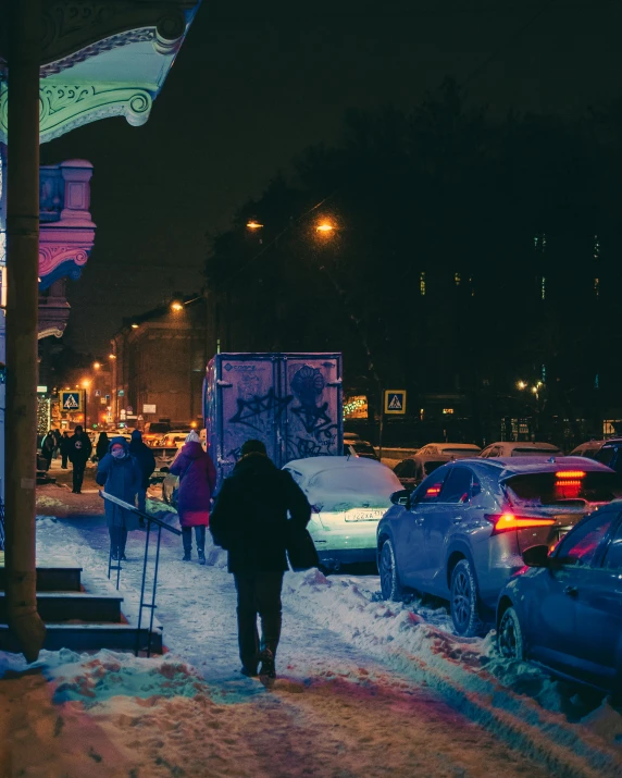 cars are parked on the side of a snow covered road as people walk down the sidewalk