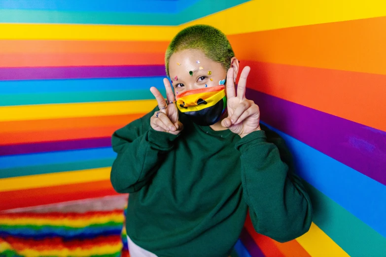 a young woman making a peace sign with her hands and wearing a rainbow mask