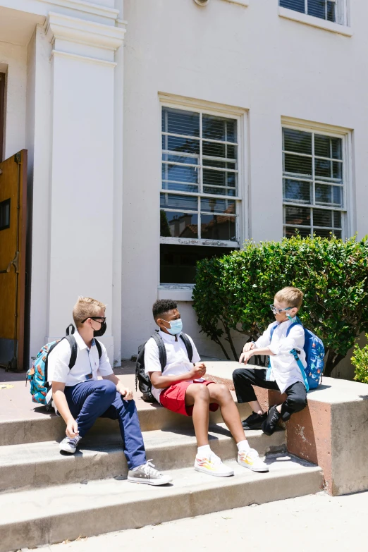 three children with backpacks sit on a stair case