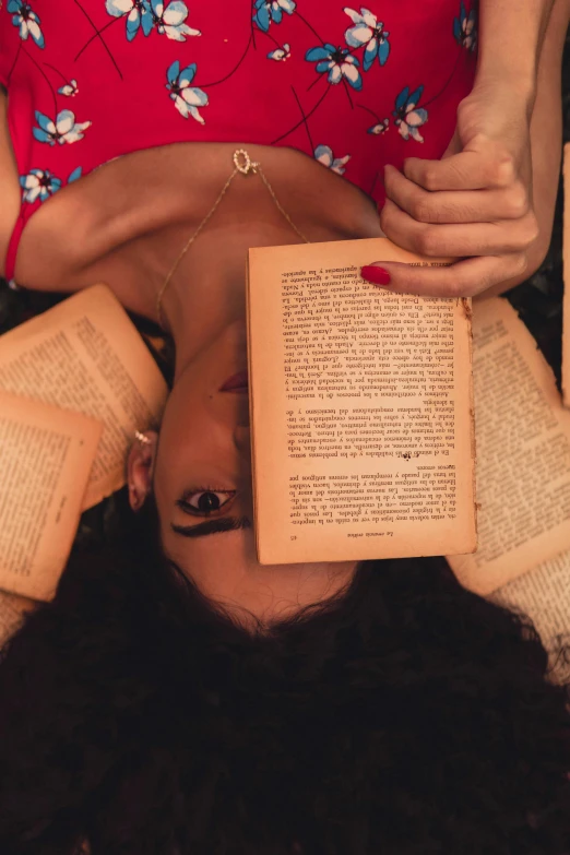 a person with a red shirt laying on her head in front of a book