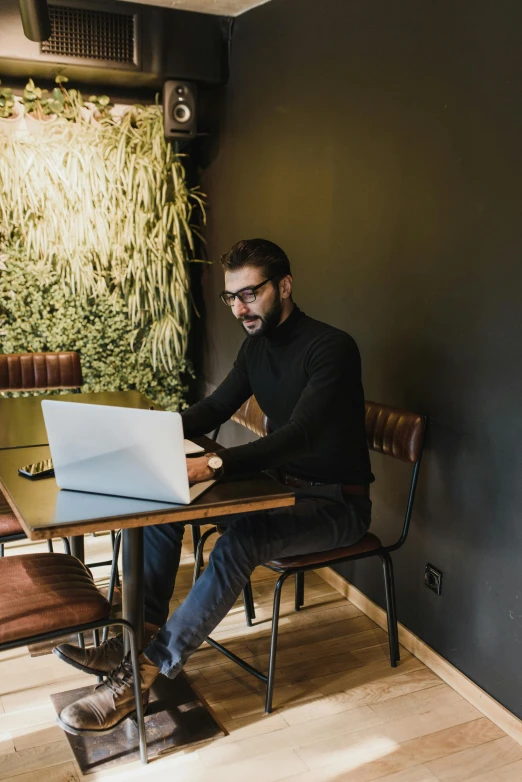 a man with glasses sitting at a table with a laptop