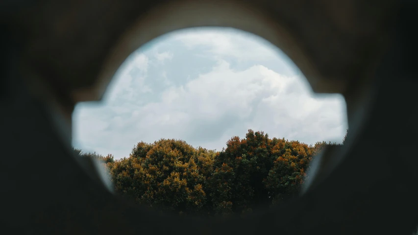 a circular opening in the side of a wall with trees seen through it