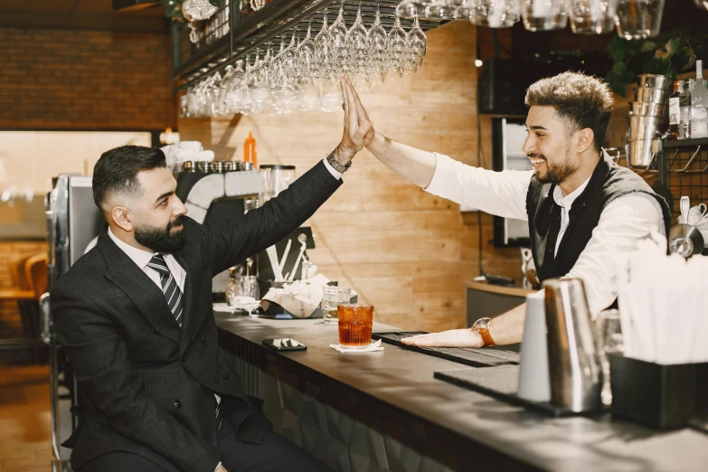 two men wearing suits and ties are standing at the bar high five