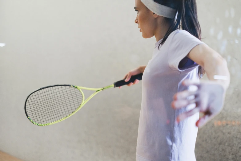 a young woman holding a tennis racket standing next to a wall