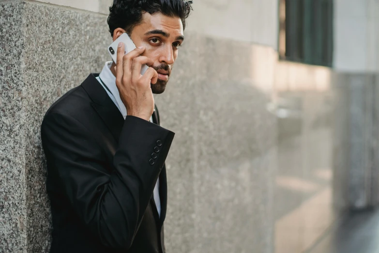 a man in suit on his cell phone leaning up against a wall