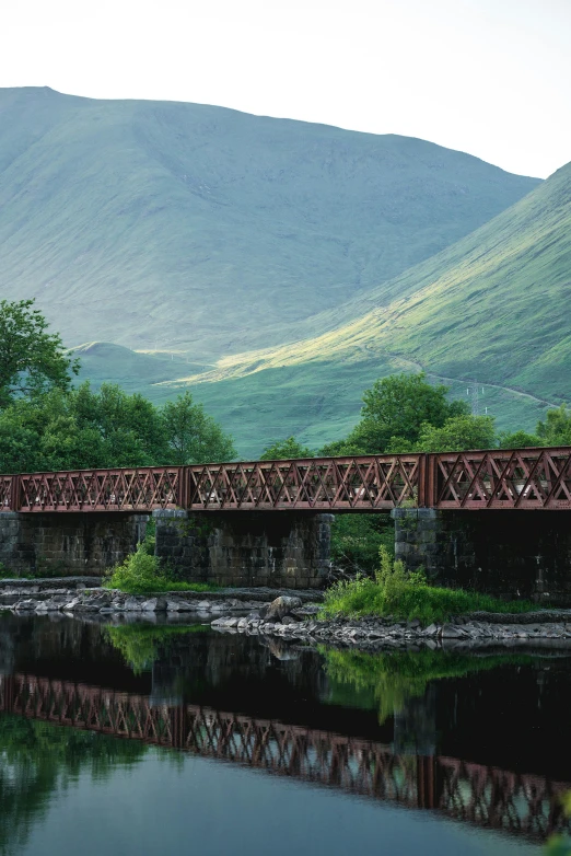 a bridge over a small river with mountains in the background