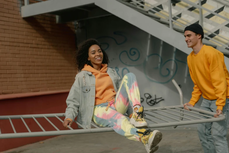 a girl holding a skateboard and standing next to a guy who is on the ground