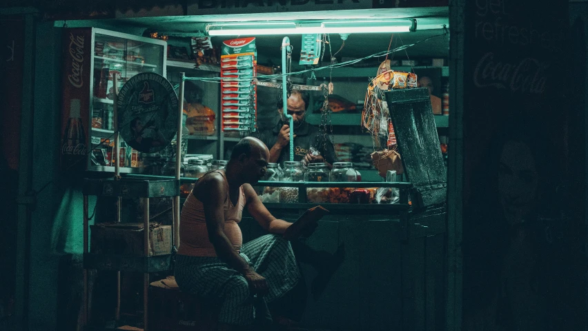 a  man sits at an open shop in the dark