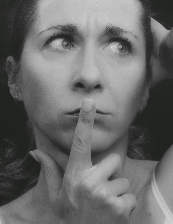 a woman is making a finger sign while holding her hands to her face