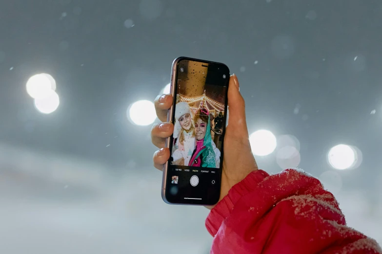 person in red jacket taking picture with cell phone on snowy day