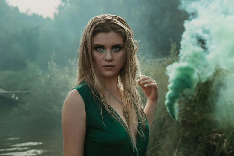 a woman with smoke in her hands standing on a riverbank