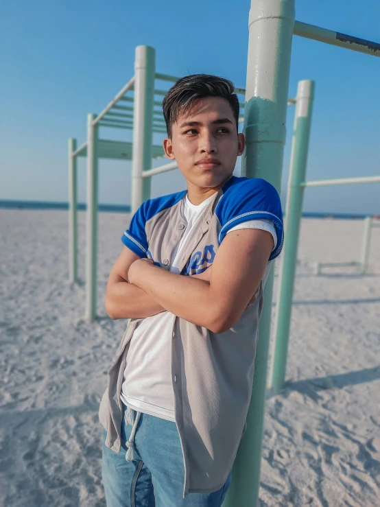 a boy leaning on a pole on a beach