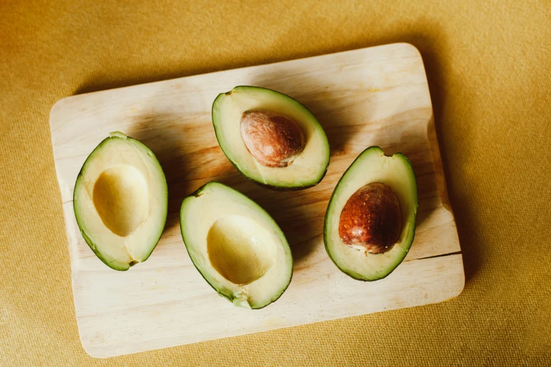 four avocados sitting on a  board, with one cut in half