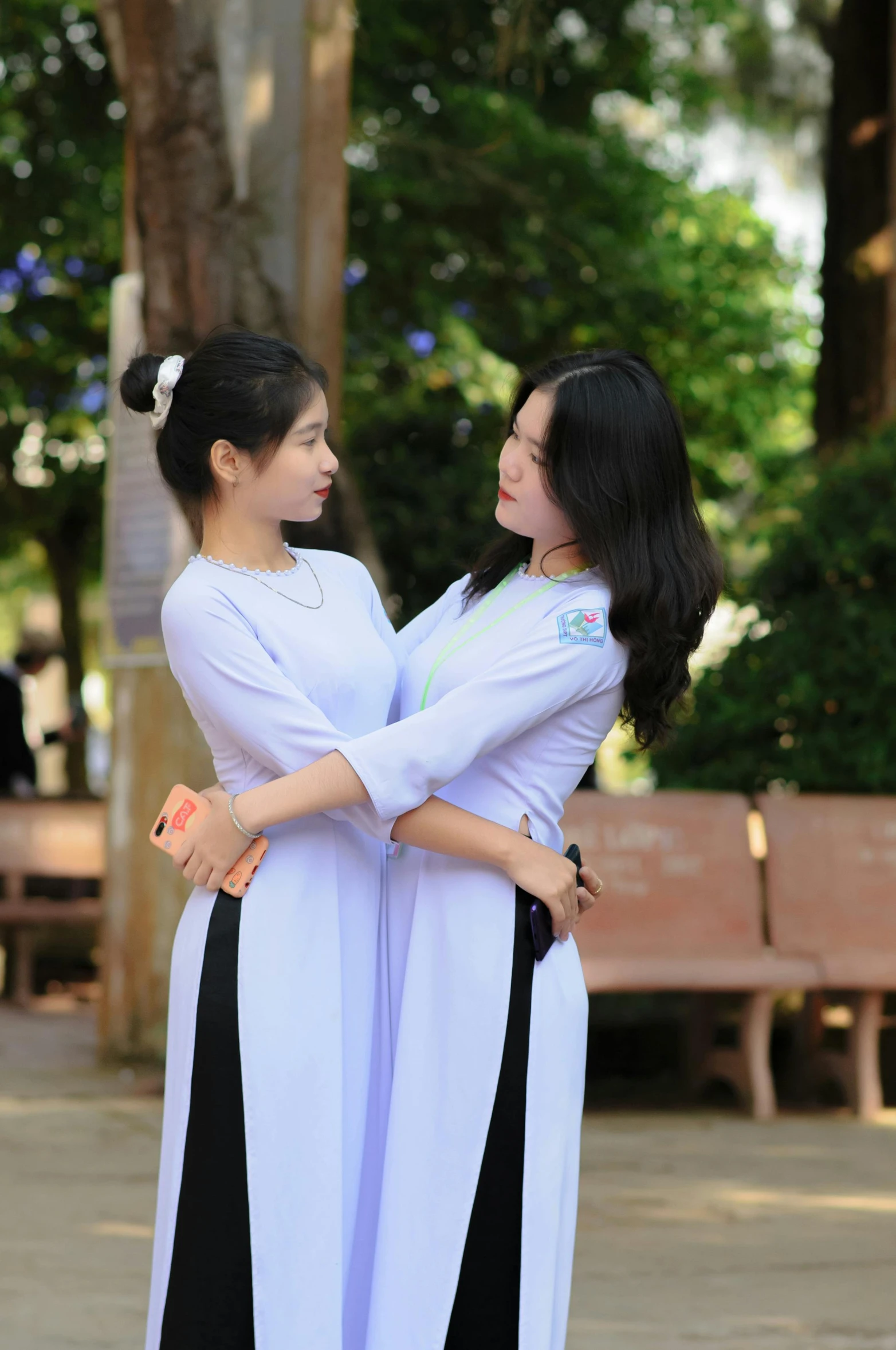 two asian women standing near one another in front of a bench