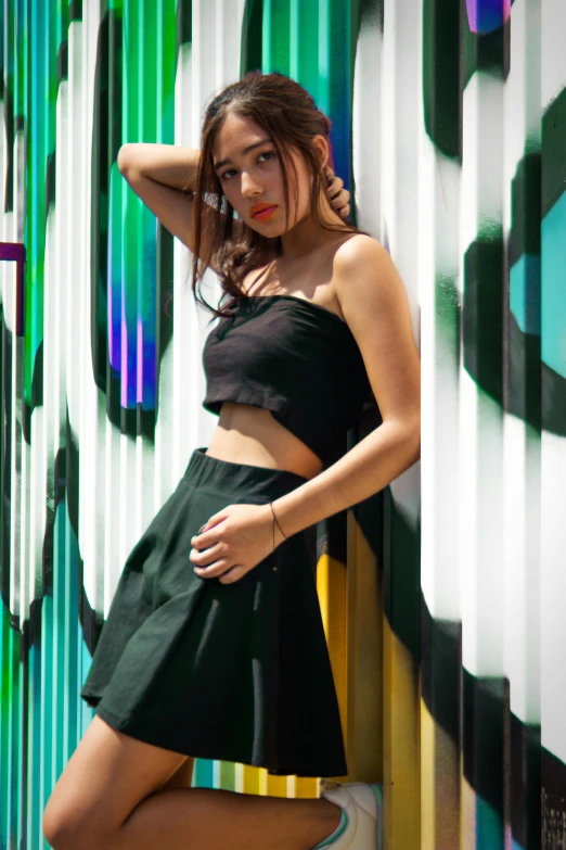 a girl in a dress leaning against a colorful wall