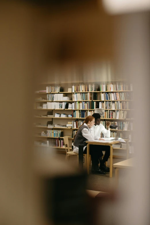 two people sit at a table in a large liry, surrounded by book cases