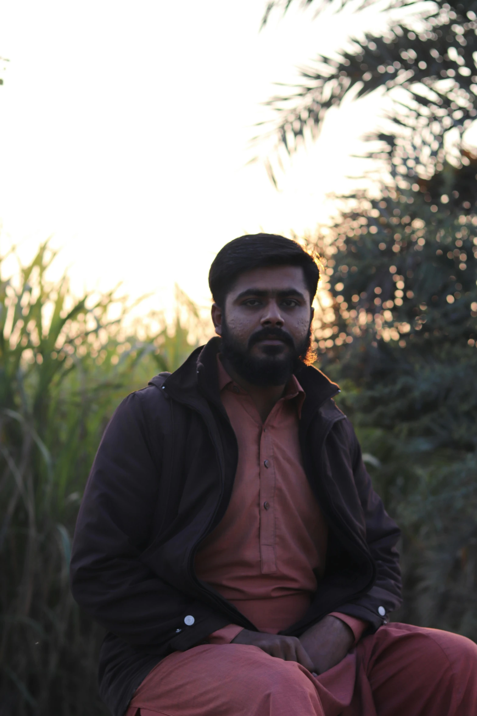 a man with beard and black jacket sitting on a rock