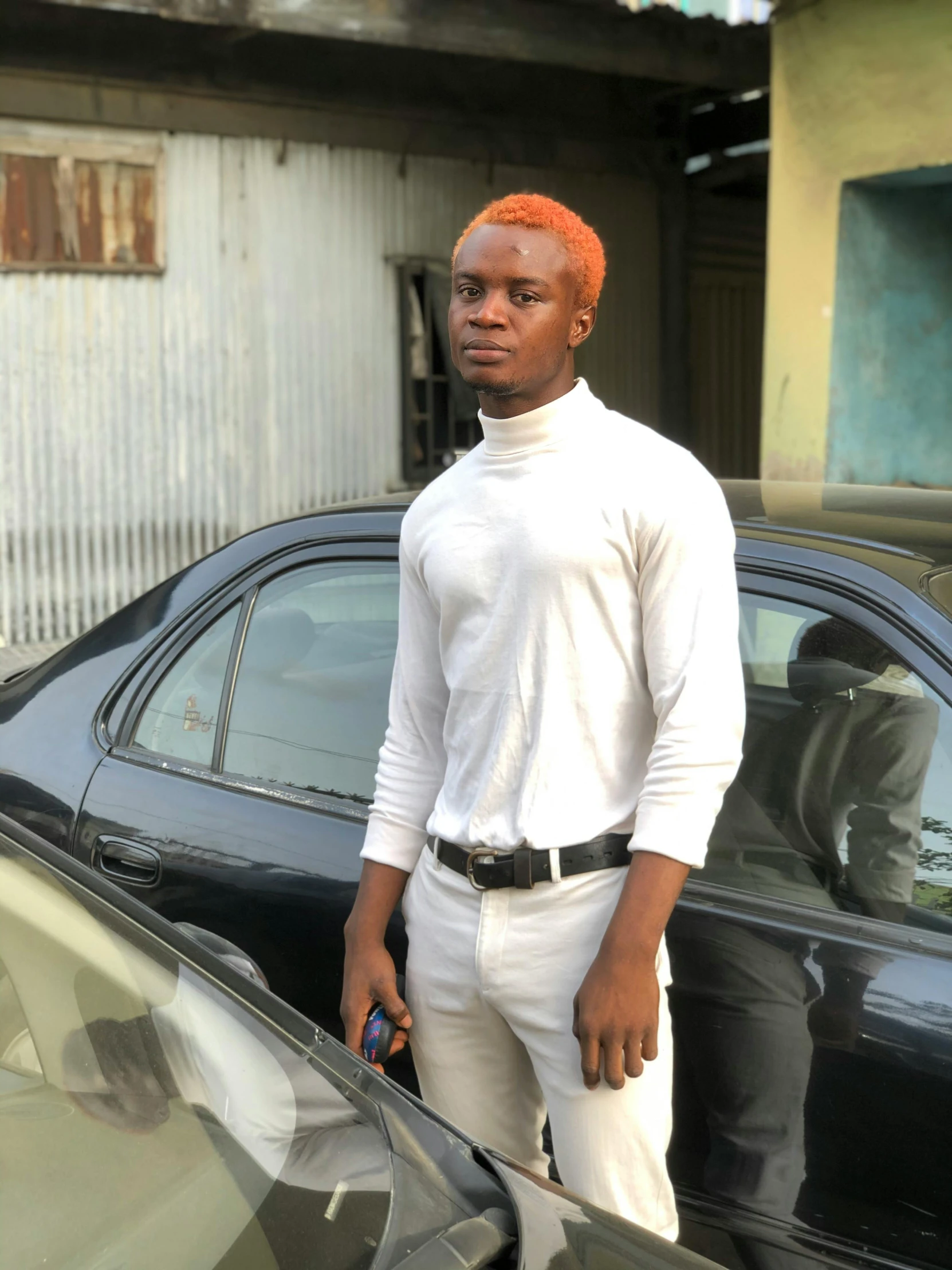 a man stands outside of his car wearing white pants