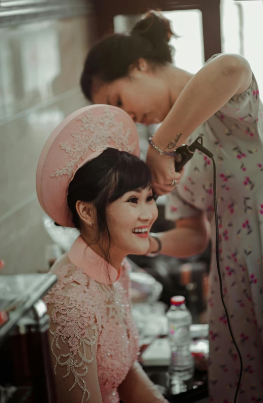 two women standing in a room with one of them is getting her hair styled