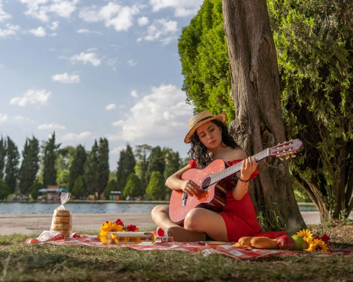 a woman is sitting under a tree playing guitar