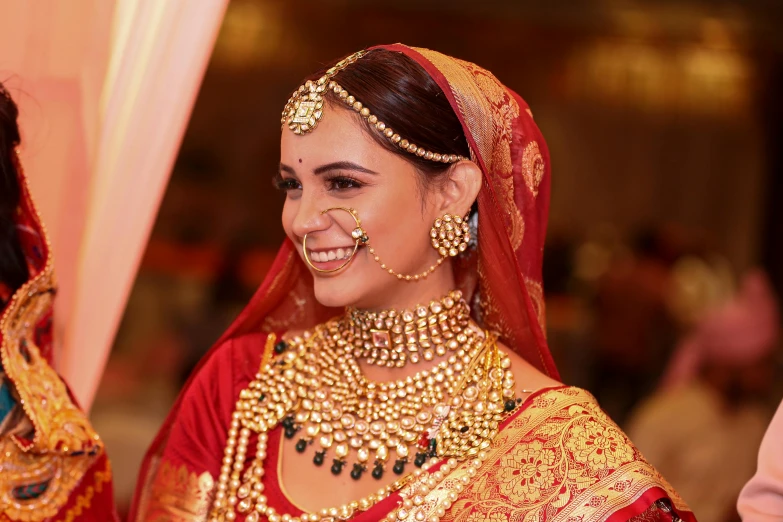 a bride in traditional red indian dress smiles as she stands before the groom