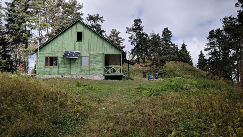 a small green house sitting on the side of a grassy hillside