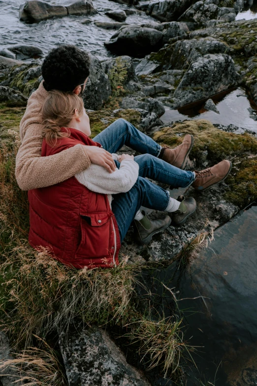 two people sitting on rocks by the water