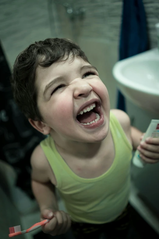 a little boy in a bathroom holding onto a toothbrush and making a weird face