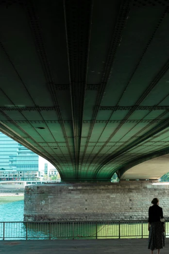 two people walking under an overpass next to the water