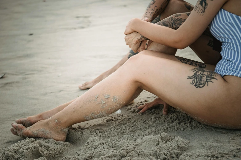 this is a woman sitting on the beach with a tattoo on her leg