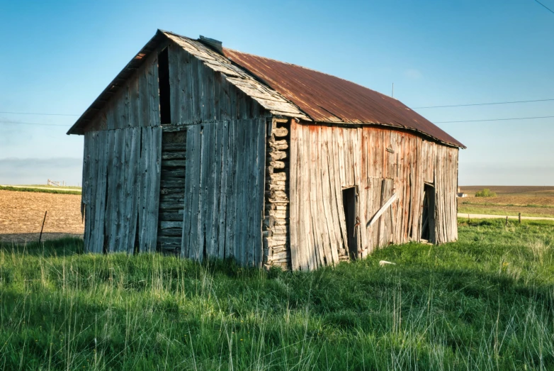 an old wooden building sitting in the middle of a green field