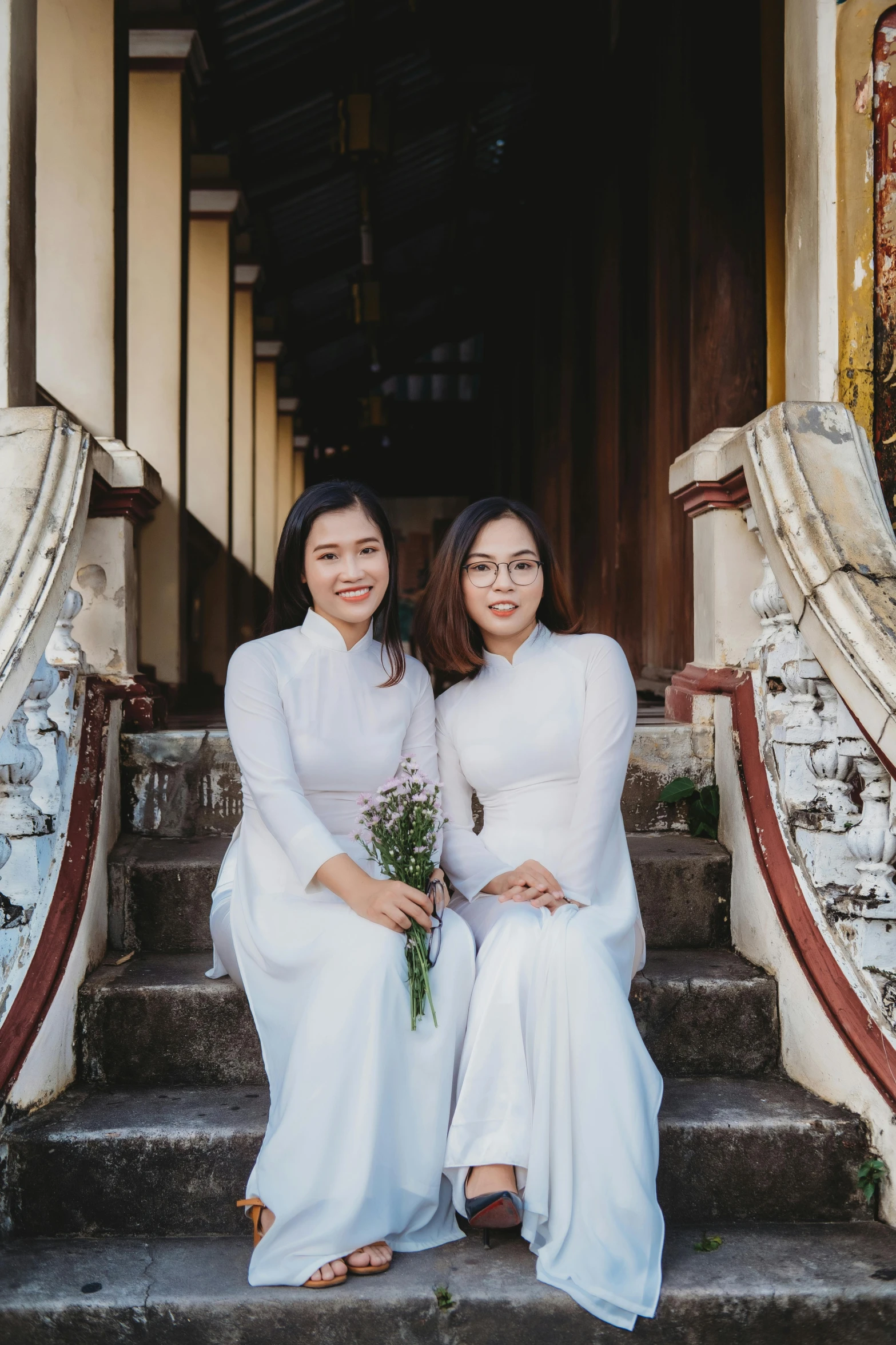 two women in white dresses are sitting on stairs