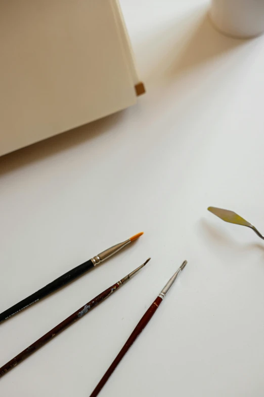 a set of four paint brushes next to a white mug