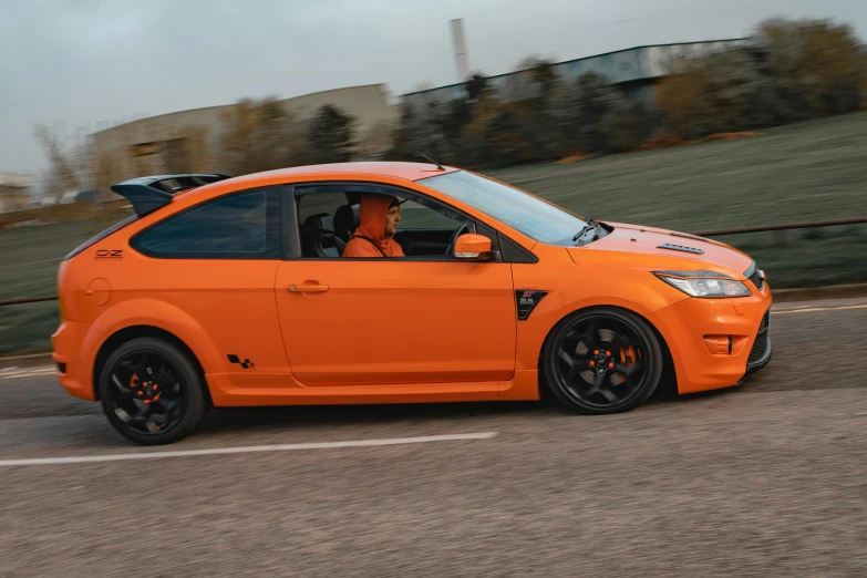 an orange car that is driving down a road