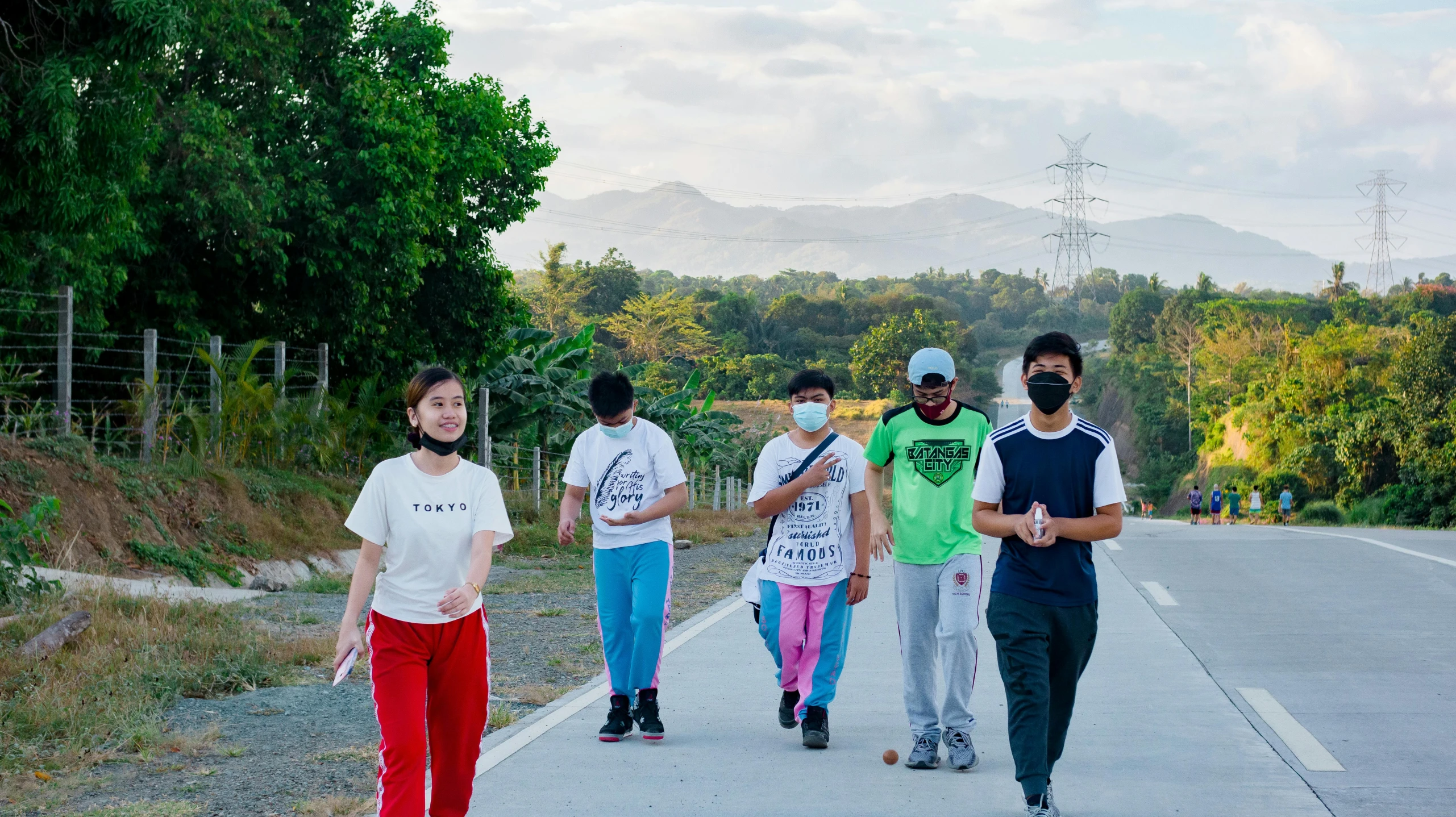 a group of teens wearing masks walking along the road