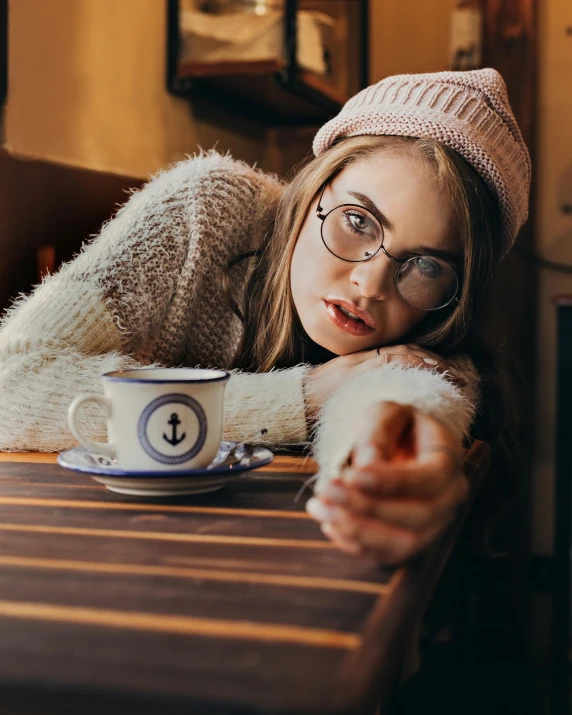 a beautiful young blonde wearing glasses leaning on a table