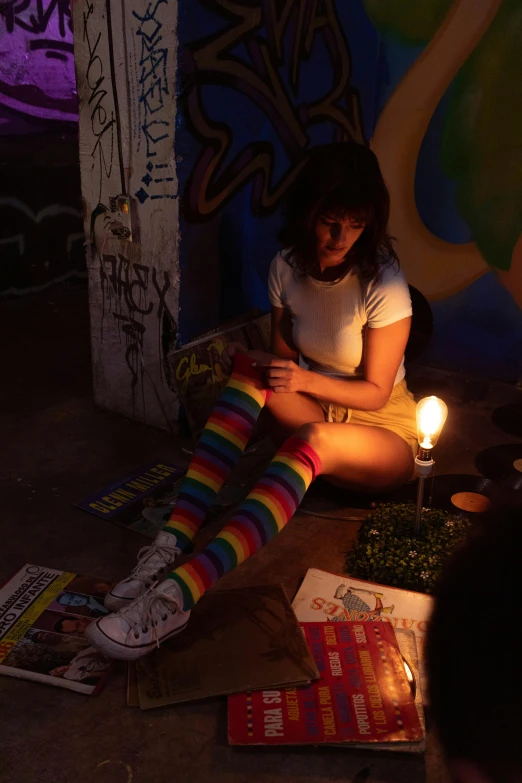 a girl sitting in the dark with a candle and many books around her