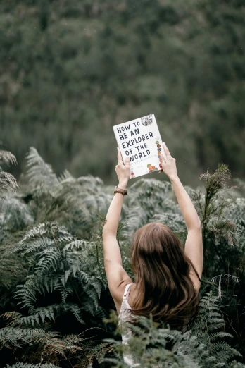 a woman holding a book in the middle of ferns