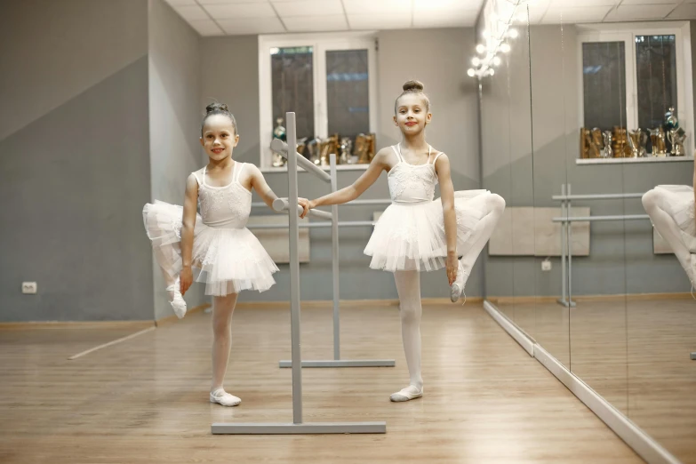 two little girls in white dresses standing on wooden floor