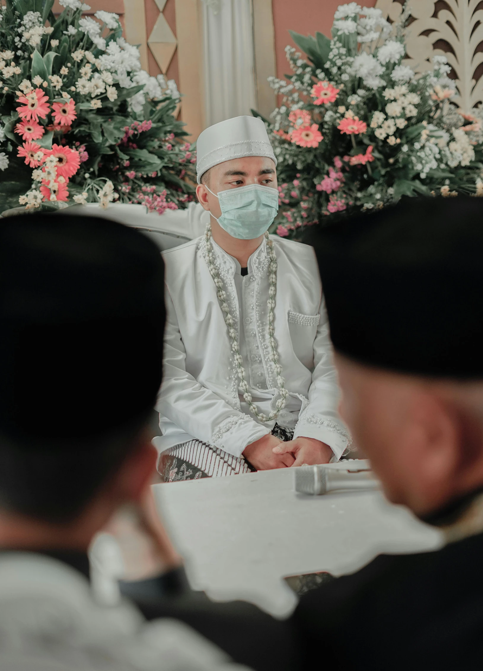 an arabic man in traditional clothing and surgical mask sitting in front of a group of men