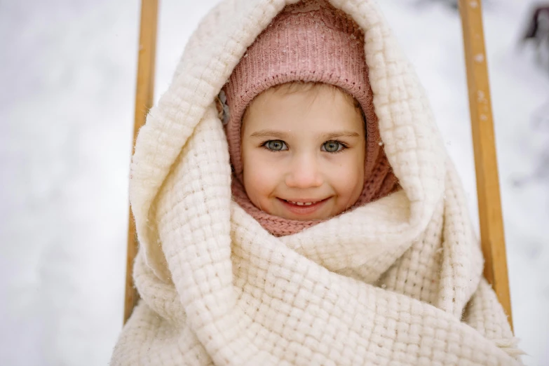 the little girl is sitting in a wooden chair covered with a blanket