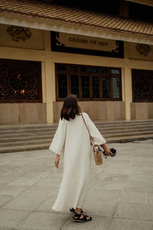 a woman in white dress walking down street with a purse