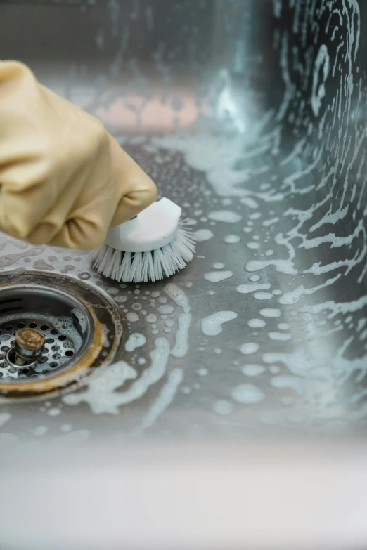 a hand in yellow rubber glove holding a brush while cleaning sink