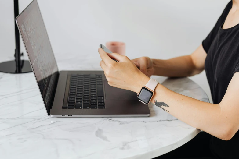 a person with a cell phone sits at a table next to a laptop computer