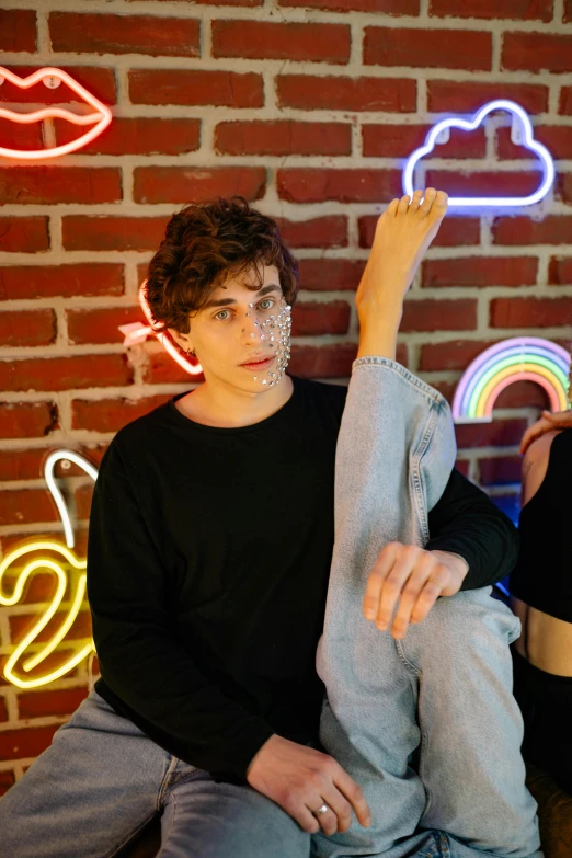 a young man wearing blue jeans and a black shirt, holding his arm up in the air and pointing towards neon signs behind him