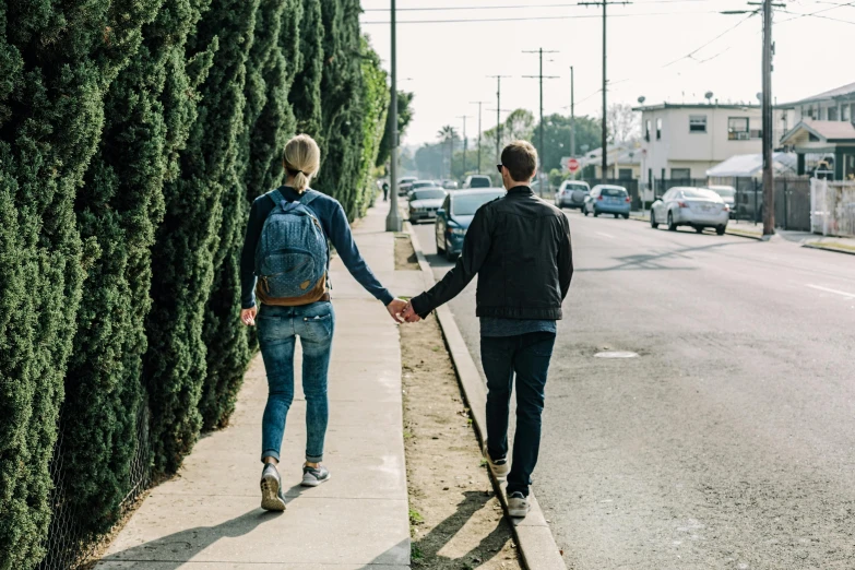 two people hold hands while walking down a sidewalk next to a city street