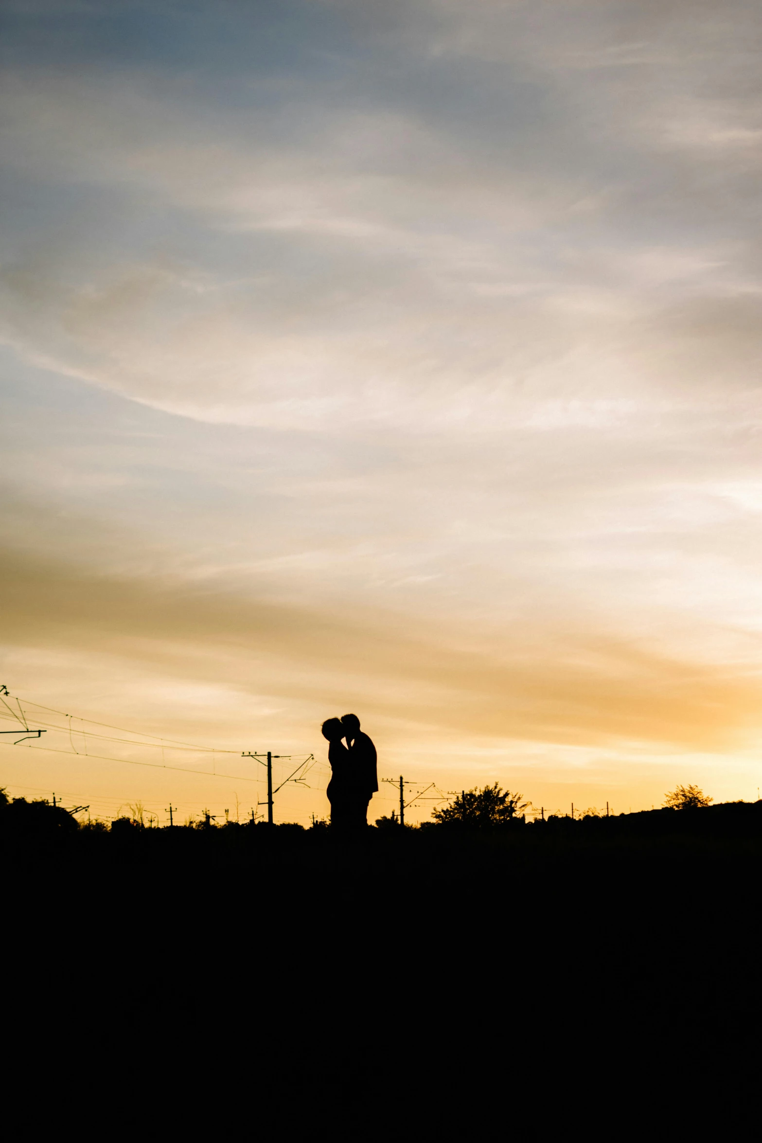 two people looking out at the sunset while a man is flying a kite